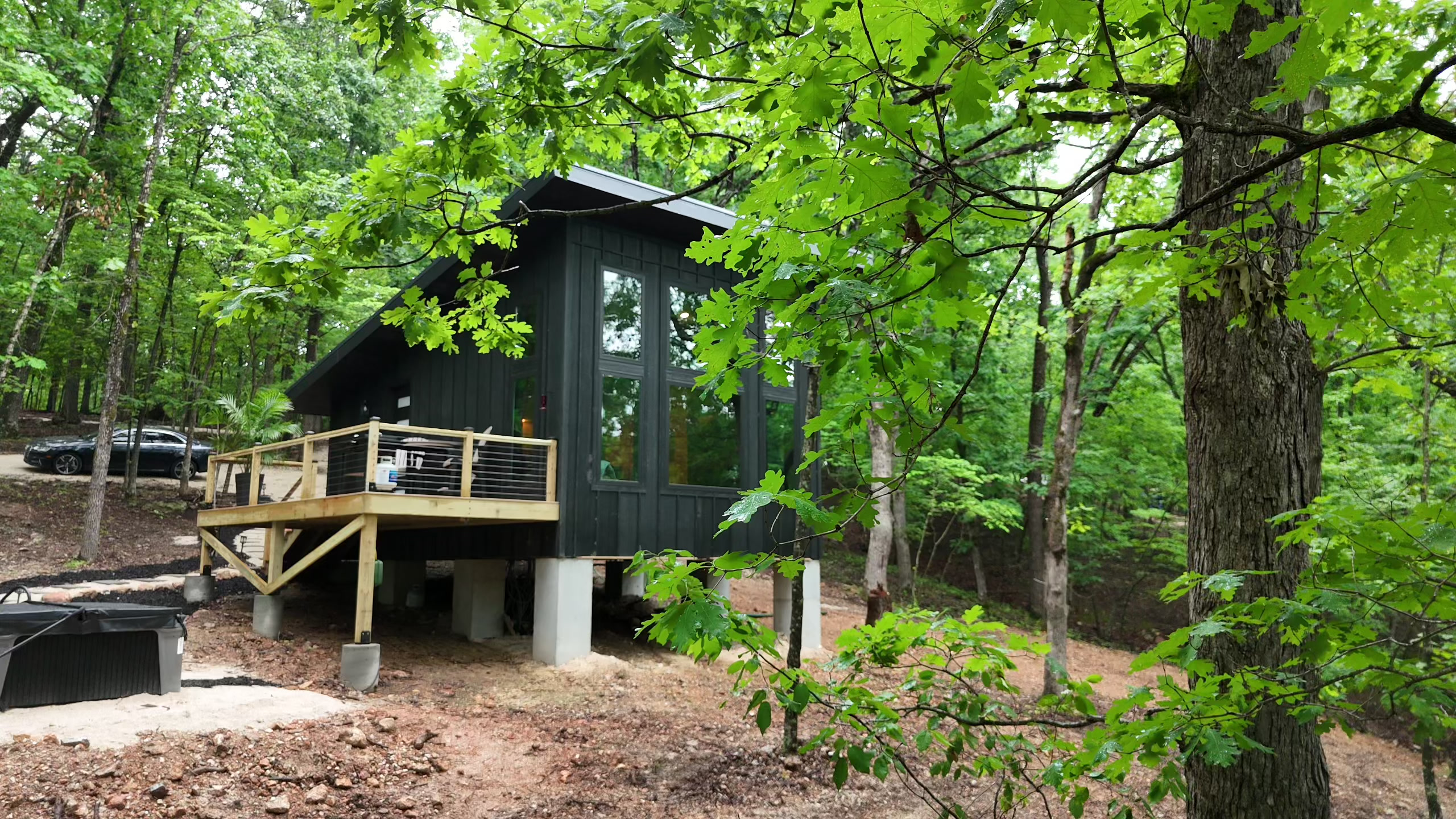 Black cabin on stilts nestled in lush green forest with wooden deck