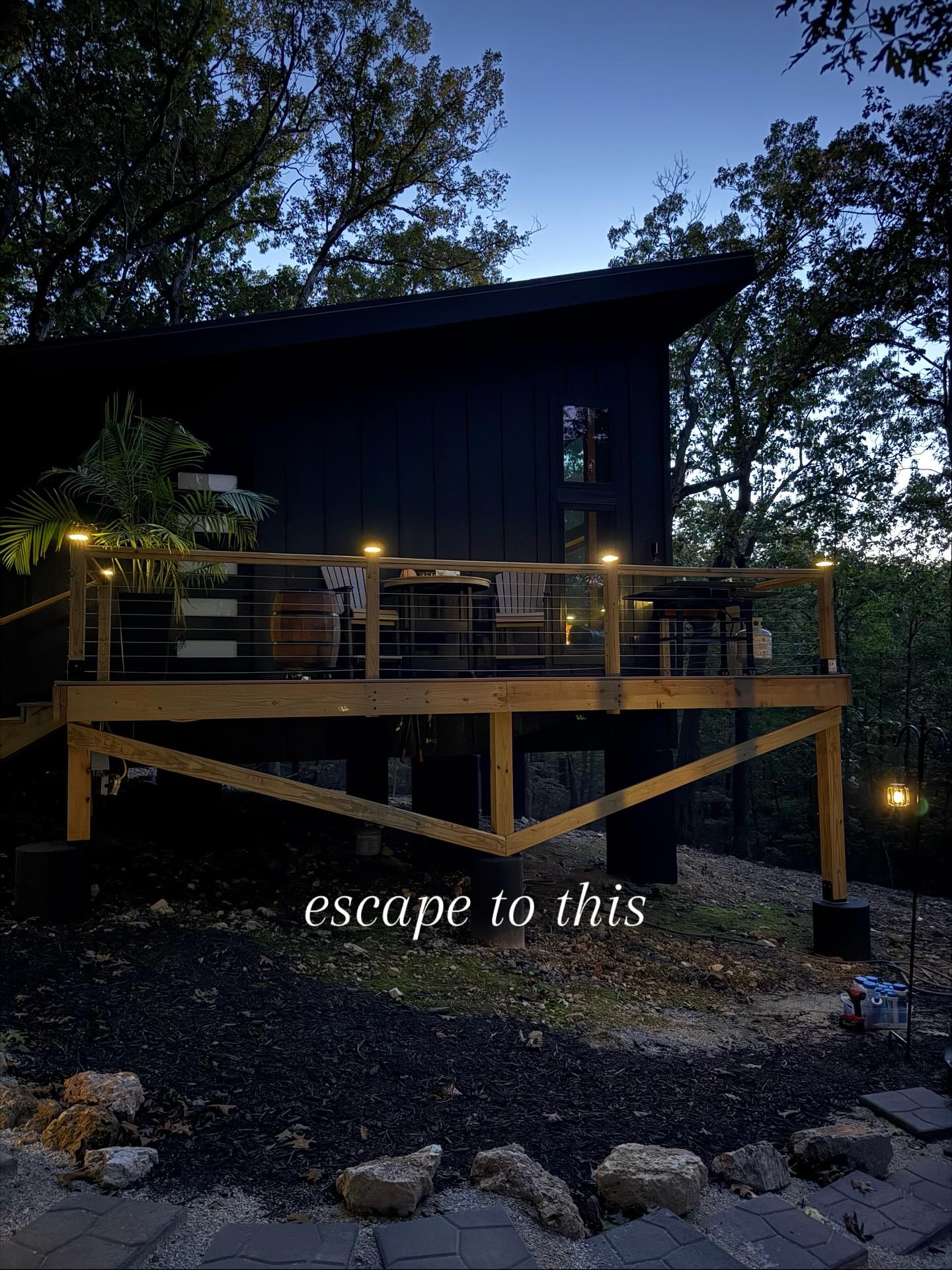 Modern black cabin with wooden deck nestled in wooded area at twilight