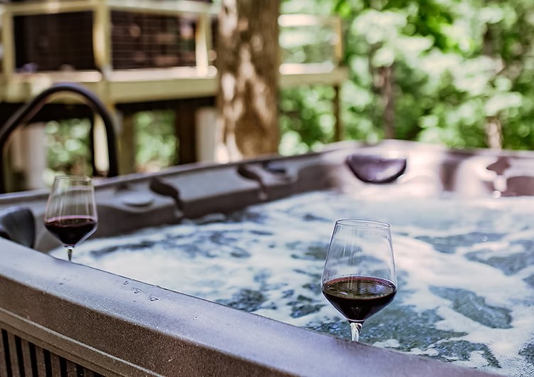 Red wine glasses beside hot tub with blurred green garden background
