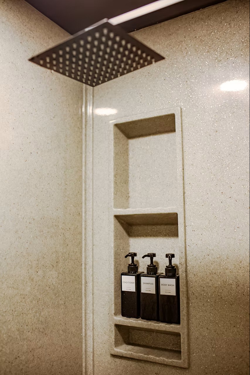Minimalist shower with rain showerhead and labeled toiletry bottles