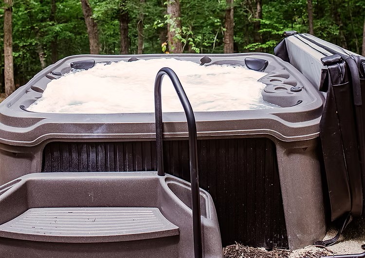 Hot tub with foamy water placed outdoors in a wooded forest setting