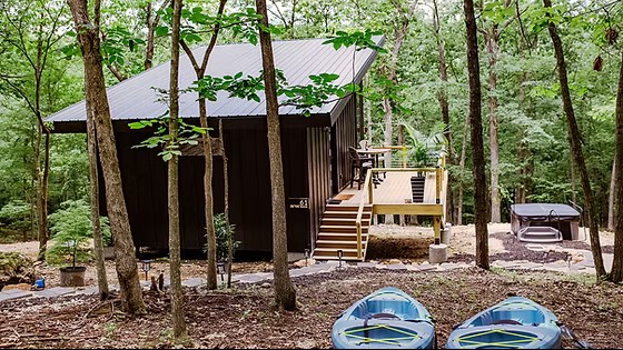 Wooden cabin with deck in forest, kayaks in foreground, peaceful woodland setting