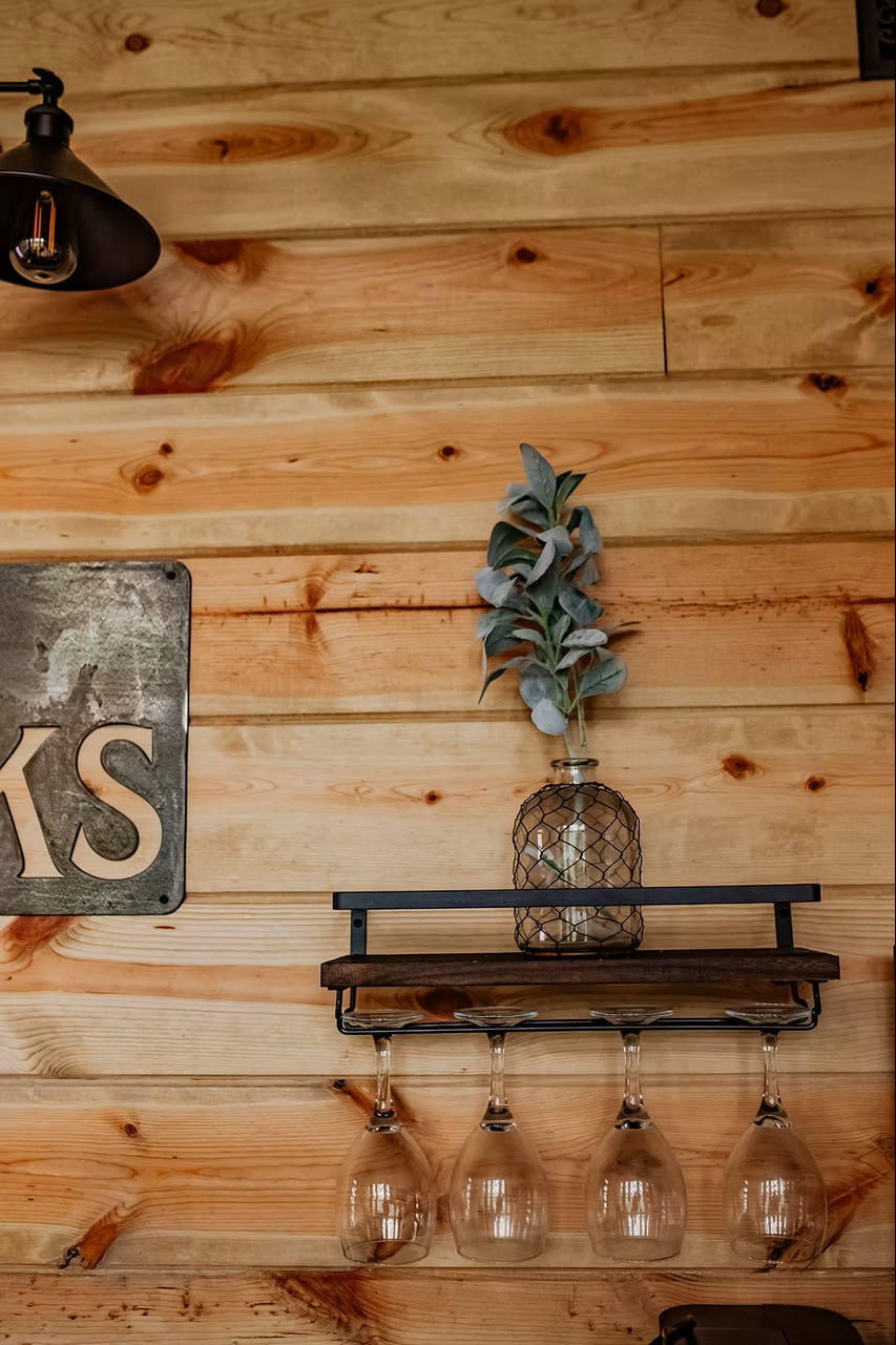 Rustic wooden wall with wine glasses, shelf, lamp, and decorative vase