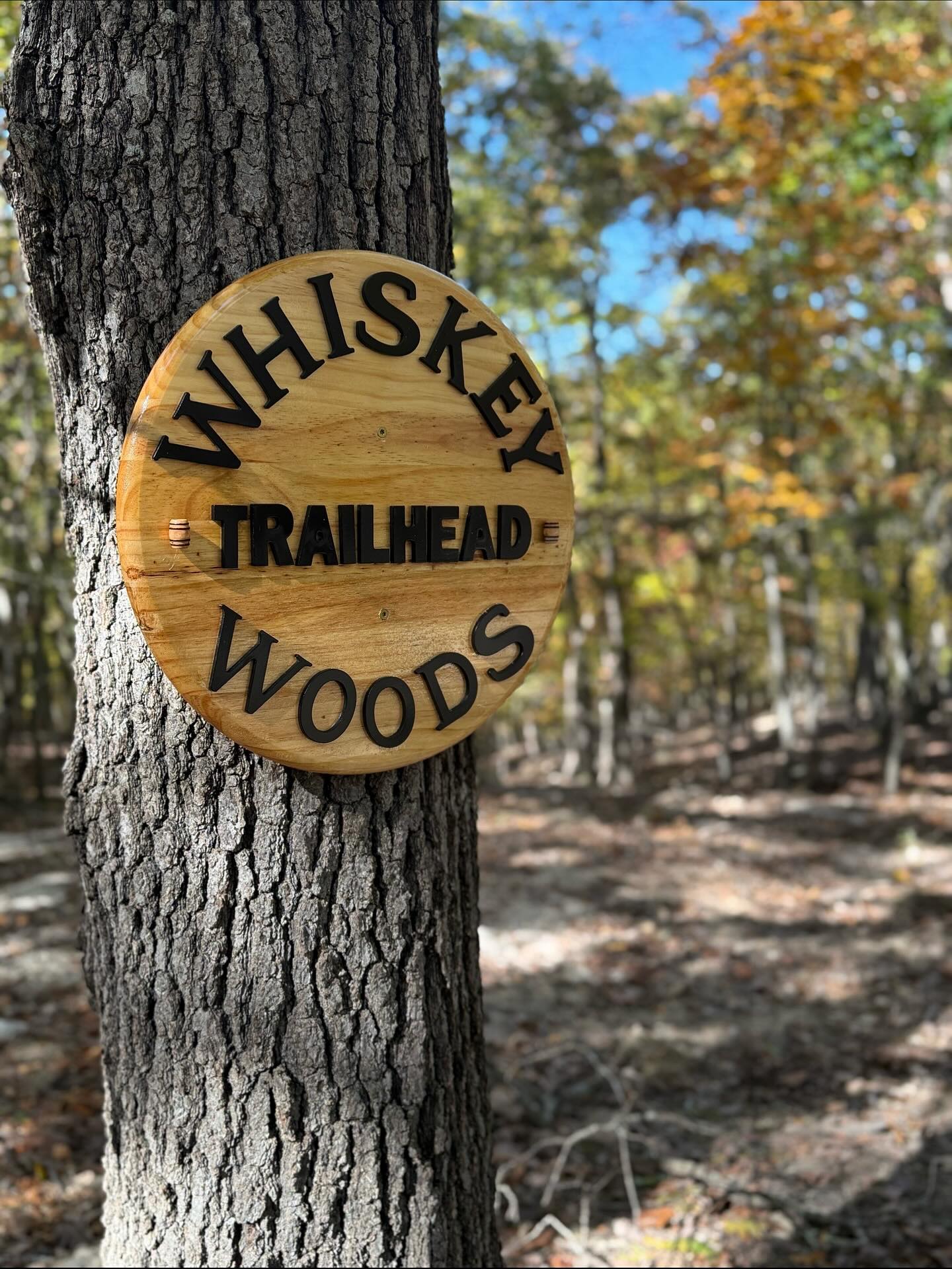 Wooden Whiskey Woods Trailhead sign mounted on a tree trunk in forest