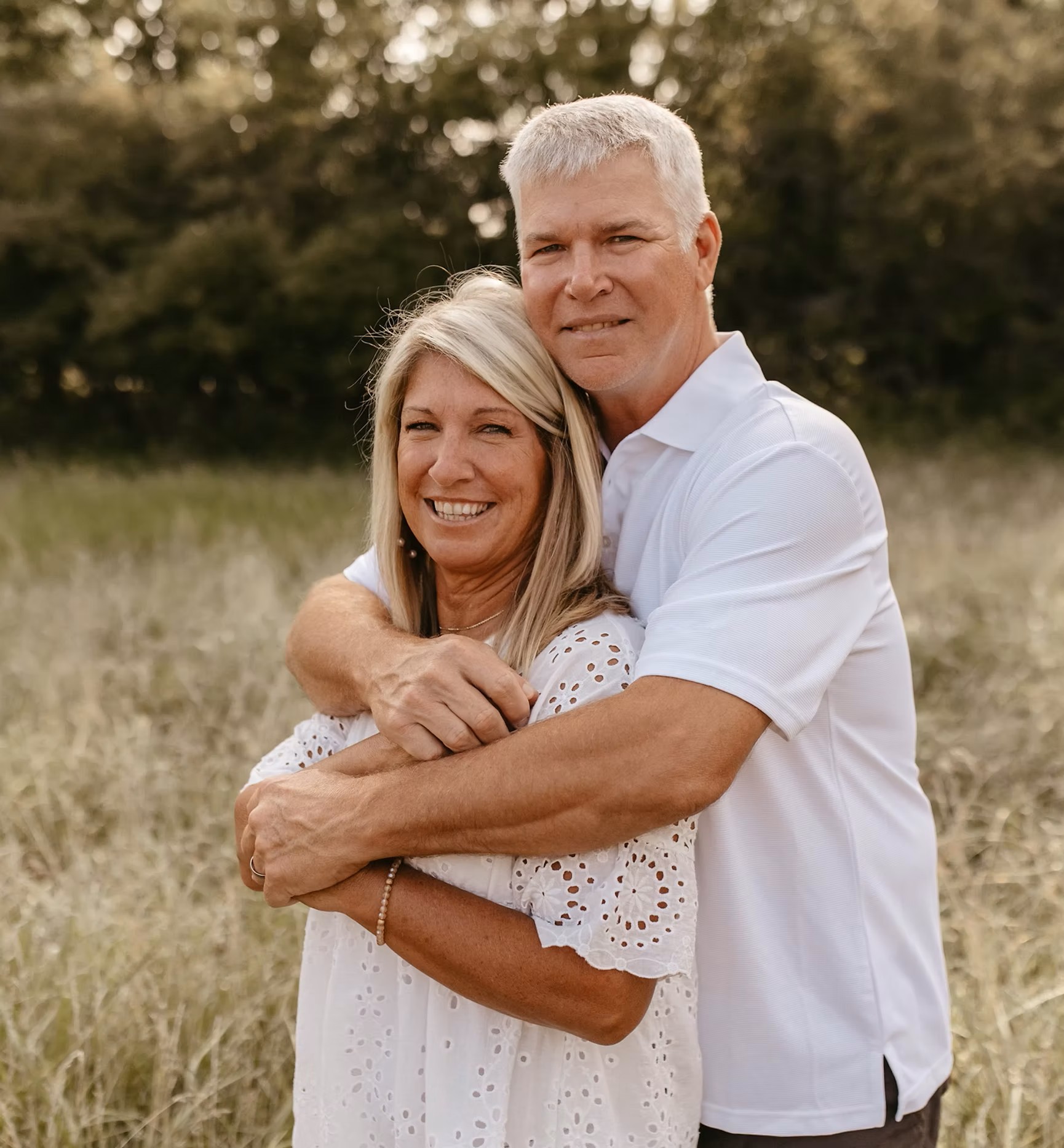 Middle-aged couple embracing in grassy field, wearing white clothing