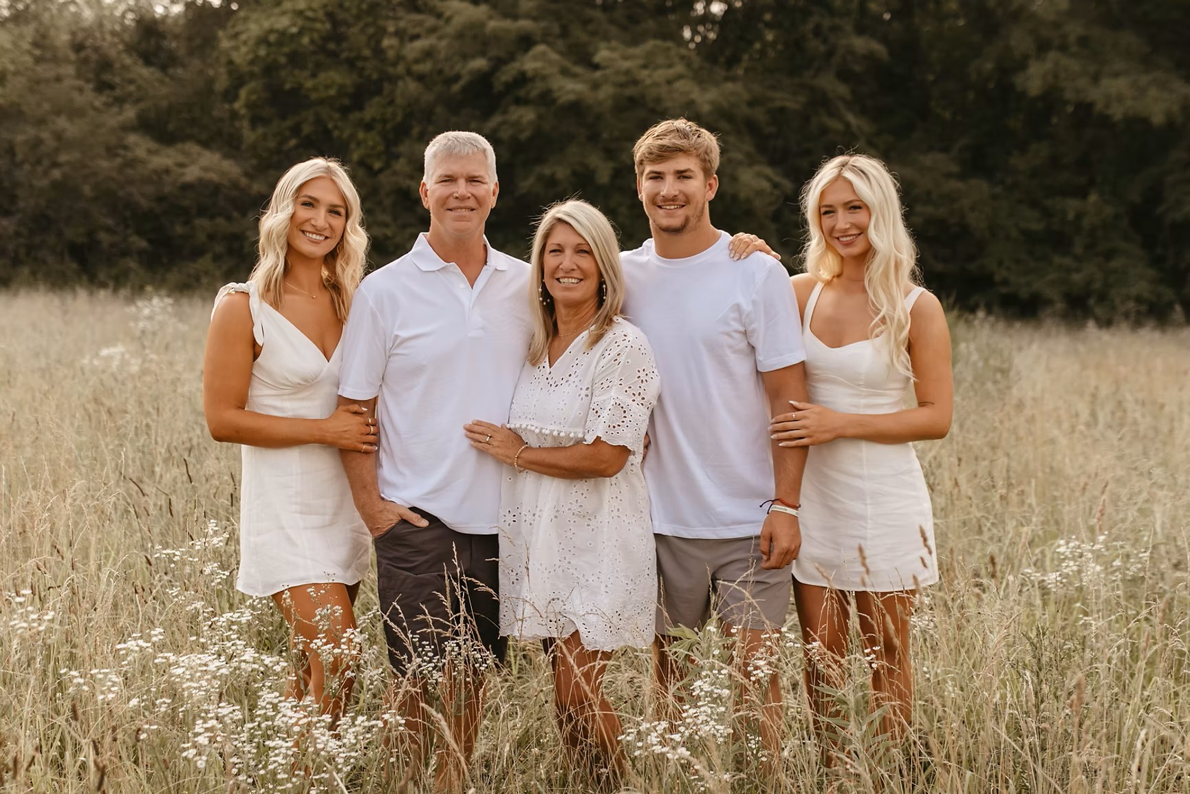 Family of five in white outfits posing in a wildflower meadow
